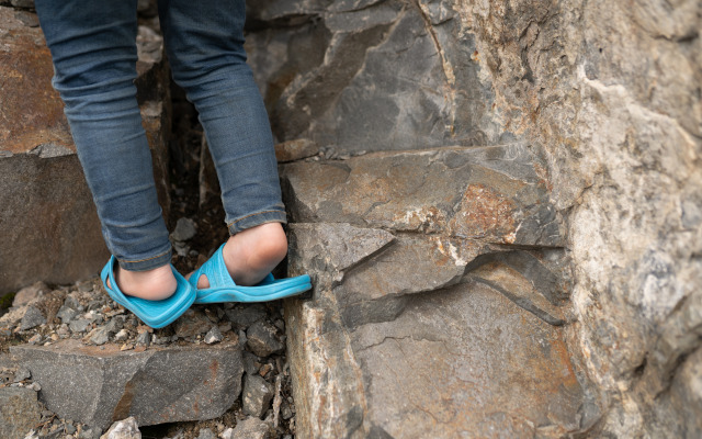 a child tries to climb rocks wearing slip-on shoes