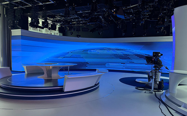 A TV studio with camera and desk in front of a curved LED backdrop